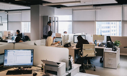 Workers in an office with a desktop computer and paperwork