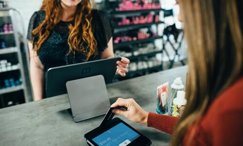 A store worker smiles at a customer in a red shirt paying for a purchase with a credit card