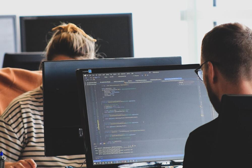 A female developer and mail developer working across from each other on desktops.