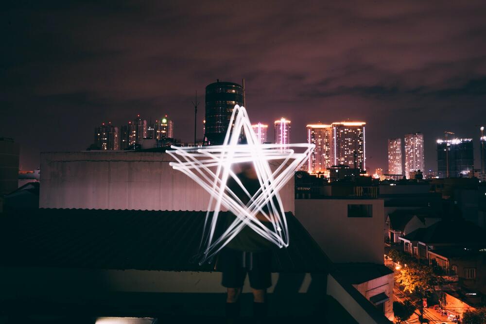 A man creates a light in the shape of a star on top of a city building with a downtown skyline in the background.